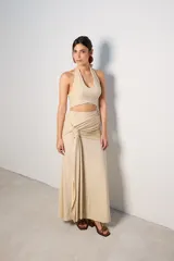 Falda larga color beige con textura brillante, corte recto y detalle drapeado en la cintura.