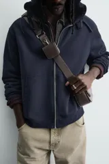 Bandolera rectangular color marrón oscuro, con solapa frontal y correa larga ajustable. Incluye un monedero pequeño en la correa.