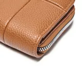 Billetera XL de diseño compacto, confeccionada en material símil cuero con textura granulada en color marrón. Presenta cierre perimetral y logo metálico de la marca en la parte frontal.