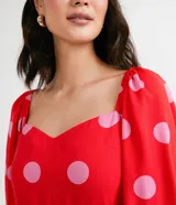 Vestido corto rojo con estampado de lunares rosas, escote cuadrado, mangas cortas abullonadas y volado en el ruedo.