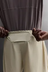 Short de running 2 en 1 color beige, confeccionado en tejido técnico ligero y elástico con malla interior integrada. Presenta cintura elástica ajustable con cordón, bolsillo trasero con cierre y aberturas laterales en el bajo.