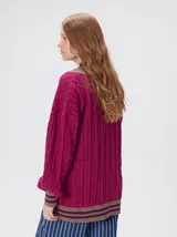 Cardigan de tejido de punto con diseño de ochos, corte oversize y mangas largas con puños acanalados. Presenta un escote en V con solapas en contraste, cierre frontal con botones y dos bolsillos delanteros con bordes en contraste. El diseño incluye detalles de rayas en los puños y en el ruedo.