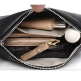 Cartera tipo baguette de color negro, confeccionada en eco cuero con textura granulada. Presenta un diseño compacto con cierre superior y una correa ajustable con detalles en tonos rojizos.