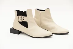 Botín de cuero negro con elásticos laterales, aplique metálico con ojales y cierre lateral con cremallera. Taco cuadrado desfasado de 3 cm.