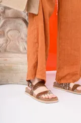 Sandalia negra de plataforma gruesa con dos tiras anchas ajustables con hebilla. Una de las tiras tiene un estampado de vaca blanco y negro.