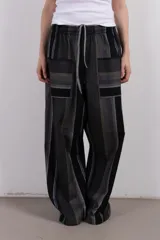 Pantalón de corte amplio confeccionado en tejido seersucker con textura rayada en tonos grises, negros y celestes. Presenta bolsillos laterales con apliques rectangulares en contraste y cintura elástica con cordón ajustable.