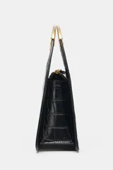Bolso de mano negro con textura de cocodrilo en relieve, doble asa metálica dorada y cadena bandolera extraíble. Cuenta con cierre de cremallera y bolsillo interior con cremallera.