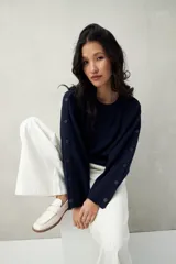 Sweater de tejido liso color azul marino, con cuello redondo y mangas largas acampanadas adornadas con una hilera de botones a tono a lo largo del lateral.