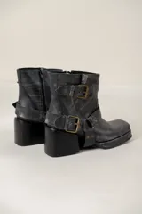 Botas cortas de cuero negro con acabado desgastado, punta cuadrada y taco bloque. Presentan un diseño versátil con estribo desmontable decorado con hebillas metálicas y tachas, permitiendo dos estilos diferentes en un mismo calzado.