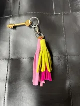Llavero con borlas de gamuza en tonos rosado, fucsia y amarillo, con aro y gancho metálico.
