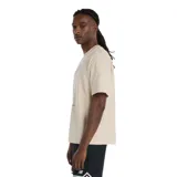 Remera de algodón color beige con cuello redondo y manga corta. Presenta un estampado gráfico central en tonos oscuros que representa a un jugador de básquet lanzando al aro, con un detalle en color rojo en la pelota y el logo de la marca en la parte inferior del diseño.