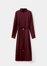 Vestido midi de tejido satinado en color bordó, con cuello alto, manga larga y diseño recto. Presenta una abertura frontal en el bajo y un cinturón ajustable con detalle metálico en la cintura.