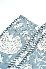 Bolso tipo tote bag acolchado, con estampado floral en tonos rosados y marrones sobre fondo blanco. Posee asas de hombro y ribetes con diseño de rayas rojas y blancas.