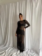 Vestido largo de encaje negro con transparencias, mangas largas y cuello redondo, acompañado de un top y un short interior a juego.