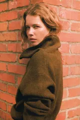 Buzo de punto acanalado en color verde oscuro, con cuello elevado y cierre frontal parcial. Presenta diseño de hombros caídos y terminaciones acanaladas en puños y bajo.