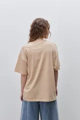 Remera blanca de calce relajado y silueta amplia, con cuello redondo, mangas cortas y estampa gráfica frontal de un cangrejo sobre franjas en tonos rosado y rojo.