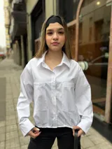 Camisa blanca de manga larga con sutiles rayas verticales, cuello camisero, cierre frontal con botones y dos bolsillos frontales con solapa.