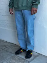 Jean azul claro de corte amplio, estilo carpintero, con pespuntes en contraste y cierre en el tobillo.