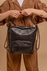 Cartera mochila de cuero sintético color negro, con diseño versátil que permite usarla como mochila o al hombro. Cuenta con un compartimento principal amplio y bolsillos frontales con cierre metálico.