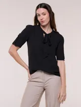 Blusa elegante negra de corte recto y tejido liviano con caída fluida. Cuenta con cuello redondo, escote en V con lazo para anudar, mangas cortas con hilera de botones forrados en los laterales y largo a la cadera con ruedo redondeado.