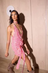 Vestido corto con diseño a rayas rojas y blancas, escote halter pronunciado, drapeado en la cadera y un lazo integrado que cuelga al costado.