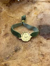 Pulsera dorada con dije redondo con la imagen de la Virgen de Fátima y cinta de terciopelo elástico color verde petróleo.