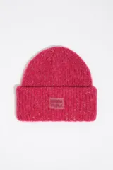 Gorro tipo beanie de punto grueso jaspeado en color fucsia, con vuelta en el borde y parche frontal de silicona con el logo de la marca.