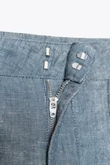 Pantalón de tiro bajo color azul con textura de lino, de pierna ancha, con bolsillos delanteros y traseros. Cierre frontal con cremallera, botón y ganchos metálicos.