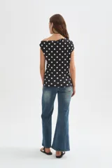 Top de poliéster negro con estampado de lunares blancos, diseño al cuerpo y cuello asimétrico de manga corta.