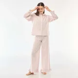 Pijama de dos piezas confeccionado en popelina con estampado de cuadros vichy en color rosa. La parte superior es una camisa de manga larga con puños con volados y cierre frontal de botones. El pantalón es de corte recto y holgado, con detalle de volados en el ruedo.