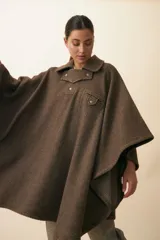 Poncho de lana fina sin teñir en color beige, con cuello camisero, cartera con broches a presión, bolsillo ojal en el pecho y diseño de corte amplio.