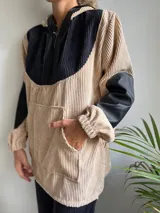 Canguro de pana color beige con capucha, mangas largas de cuero sintético negro y cierre frontal parcial con cremallera.