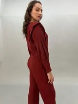 Mono largo color ladrillo de crepe de lana liviana, con corte entallado en la cintura, bolsillos laterales y mangas largas con detalle de volados en los puños. Presenta una moldería superior que enmarca los hombros como si fuera un chaleco.