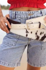 Cinto faja de cuero con estampado de vaca en blanco y negro, con hebilla metálica rectangular.