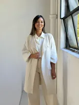 Chaleco largo de punto color crudo, con diseño abierto, sin botones y bolsillos frontales aplicados. Presenta bordes acanalados en la parte frontal y en el ruedo.