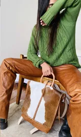 Mochila de cuero con tapa de pelo vacuno en combinación de marrón y blanco, con detalles de costuras artesanales a mano, manija superior circular y correas regulables.