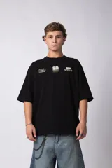 Remera de corte oversize color negro, confeccionada en algodón premium. Presenta un diseño gráfico minimalista estampado en el frente con tipografía y logotipos en color crema.