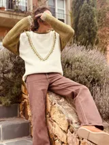 Sweater color crudo con mangas largas color verde oliva. Presenta cuello redondo y detalle de bordado con pompones en forma de V en el frente.