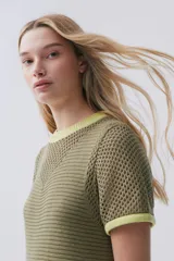 Vestido largo verde de tejido de punto calado, con escote redondo y mangas cortas. Tiene tajos laterales y ribetes en color amarillo.