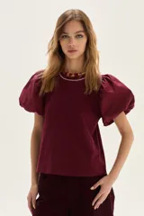Blusa con cuerpo de jersey y mangas globo (ballon) de popelina, color vino tinto. Presenta un calce recto y cuello redondo con un borde de pespunte blanco.