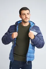 Campera puffer con diseño color block en tonos azul marino, gris y azul claro. Cuenta con capucha, cierre frontal completo, bolsillos laterales con cierre y logo estampado en el pecho.