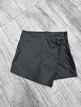 Short pollera negro de cuero sintético con corte cruzado y hebilla metálica.