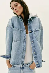 Cazadora de denim oversize con capucha gris desmontable, cuello camisero, cierre frontal con botones metálicos y bolsillos delanteros de plastrón.