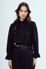 Camisa negra de manga larga con cuello camisero, frente abotonado, detalles fruncidos en el pecho y puños con volados.