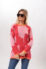 Sweater de punto con diseño geométrico abstracto en tonos rosa y rojo, con cuello redondo y puños y bajo acanalados en color naranja.