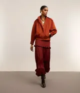 Falda midi evasé color borgoña de poliéster satinado, con cierre trasero invisible, volado en la cadera y ruedo fruncido.