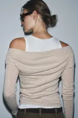 Camiseta de manga larga gris melange con cuello redondo y diseño asimétrico que simula una doble camiseta, con una capa inferior blanca visible en el cuello y el bajo.