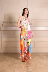 Vestido largo de seda con estampado vibrante y multicolor que incluye motivos frutales y caras sonrientes. Diseño de solera con escote halter anudado al cuello y falda amplia.