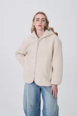 Campera de corderito con capucha, cierre frontal completo y bolsillos laterales. Presenta un diseño holgado de manga larga en color beige.