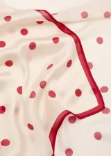 Pañuelo cuadrado de tejido satinado color beige con estampado de lunares rojos y borde rojo.